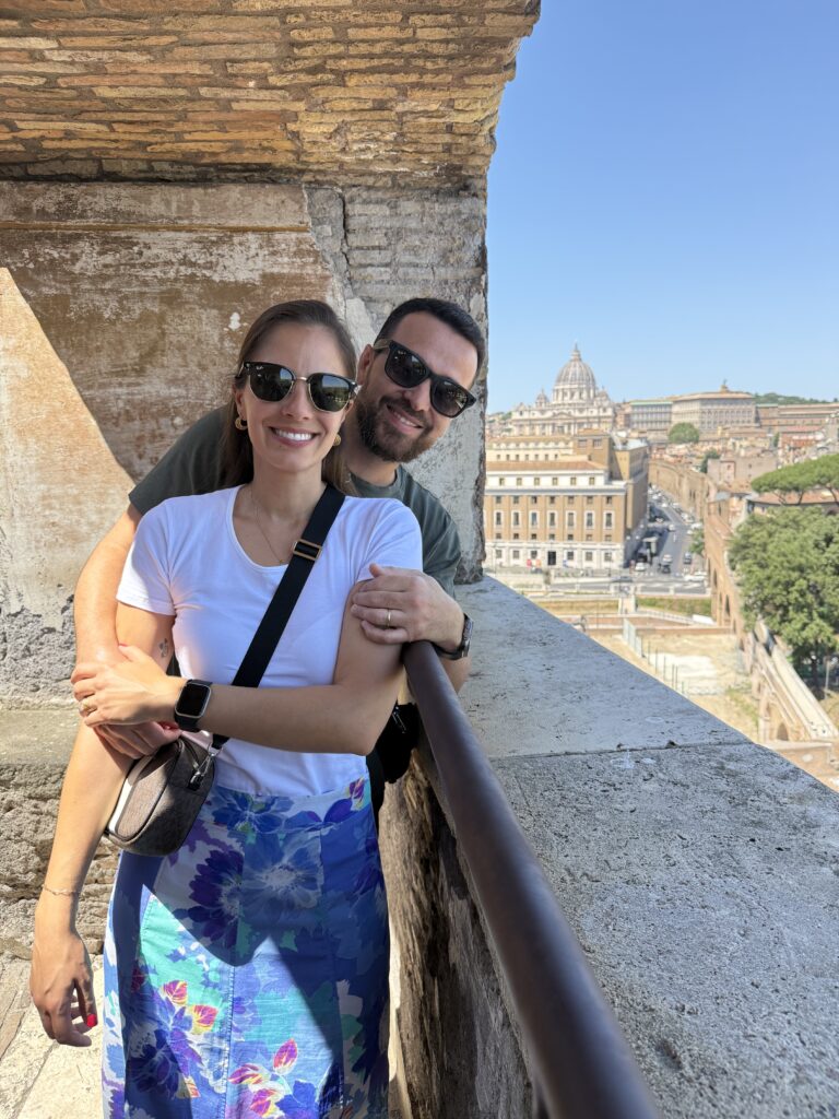 Patrícia Doneda e Leonardo Almir Rodrigues em uma janela, com o Vaticano ao fundo, em Roma