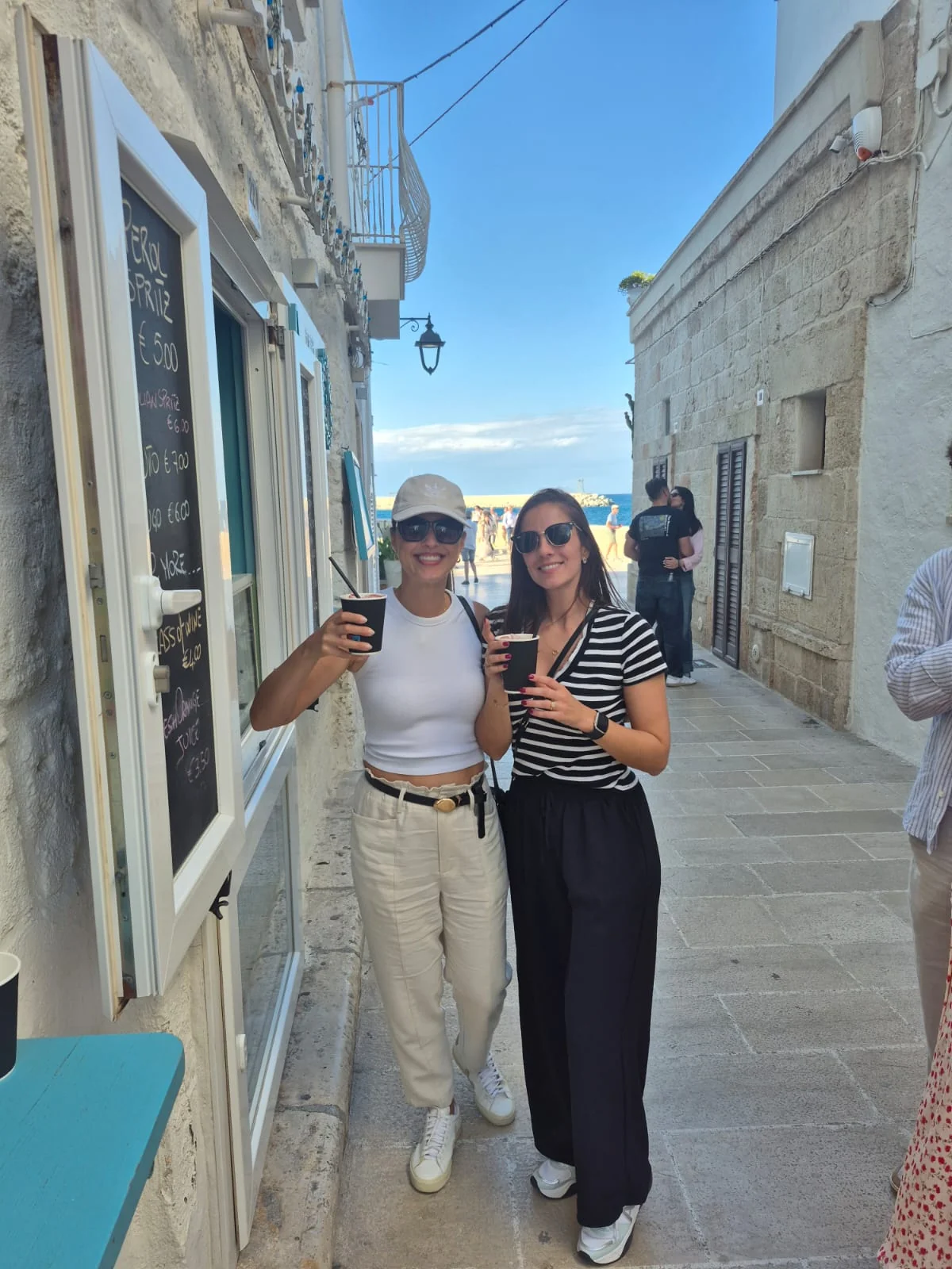 Duas visitantes com bebidas para levar durante passeio pelo centro histórico de Monopoli