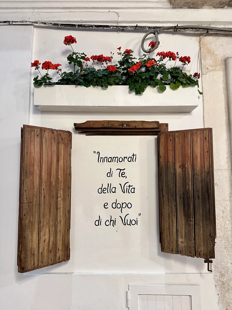 Fachada de Cisternino com portas de madeira e flores vermelhas